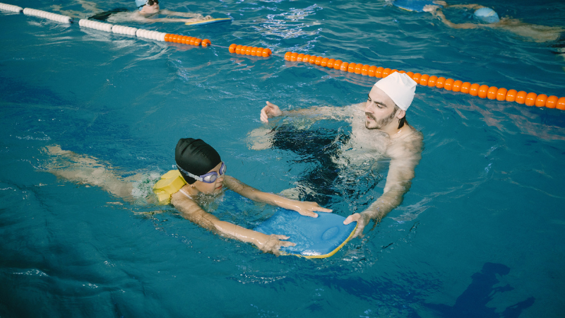 Coach teaching kid in indoor swimming pool how to swim and dive